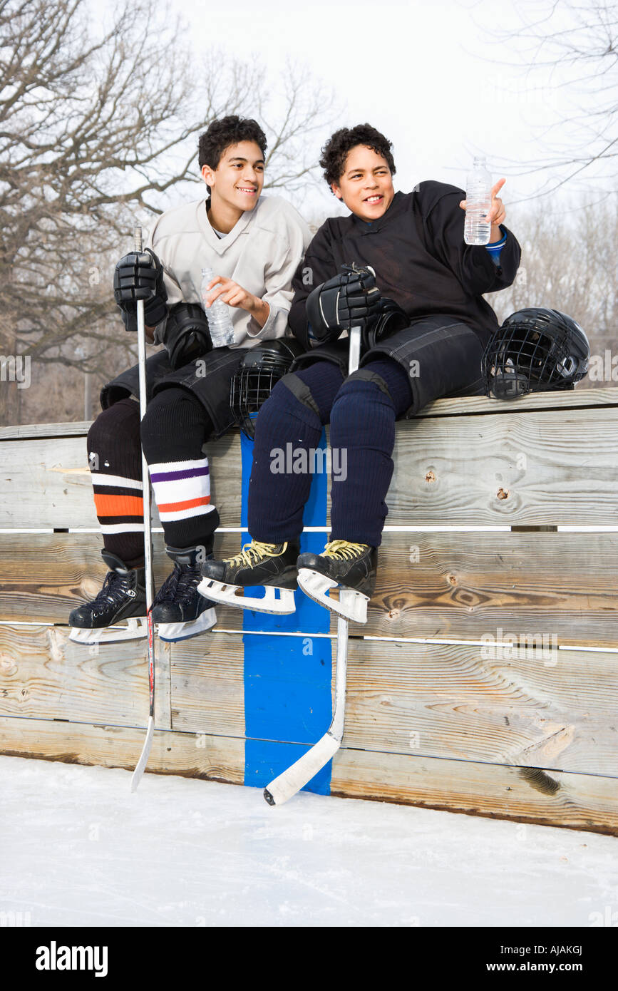 Two boys in ice hockey uniforms sitting on ice rink sidelines pointing and looking Stock Photo