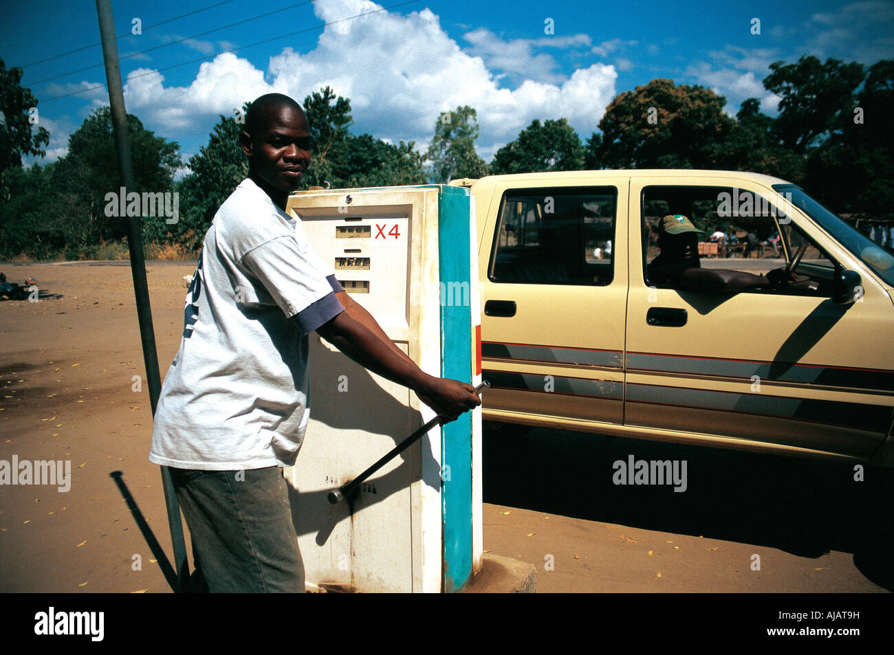 A young black African man using a hand operated petrol pump to refuel a car in Malawi Stock Photo
