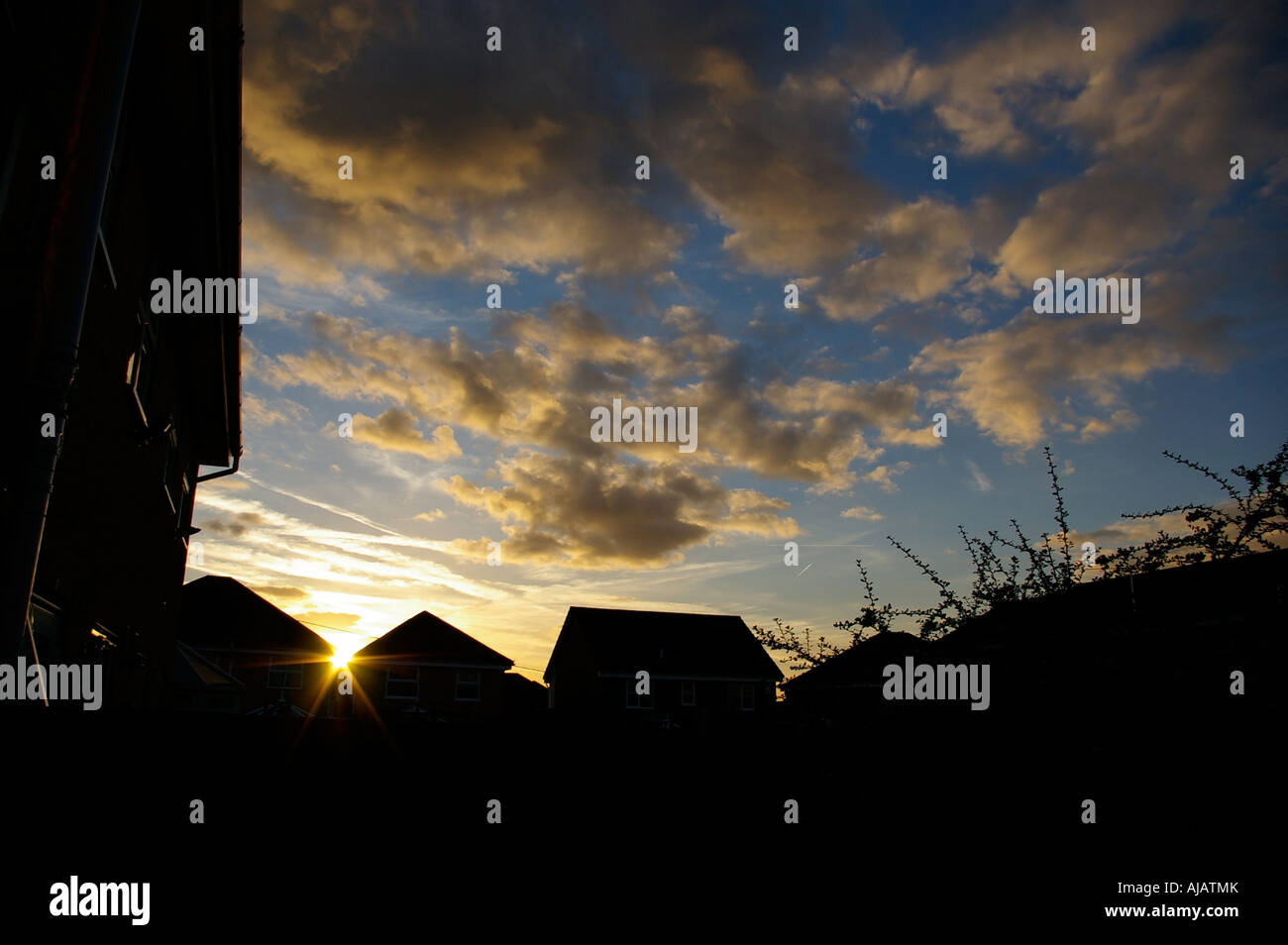 sun setting over a suburban rooftop with cloudy skies cloudy sky Stock Photo