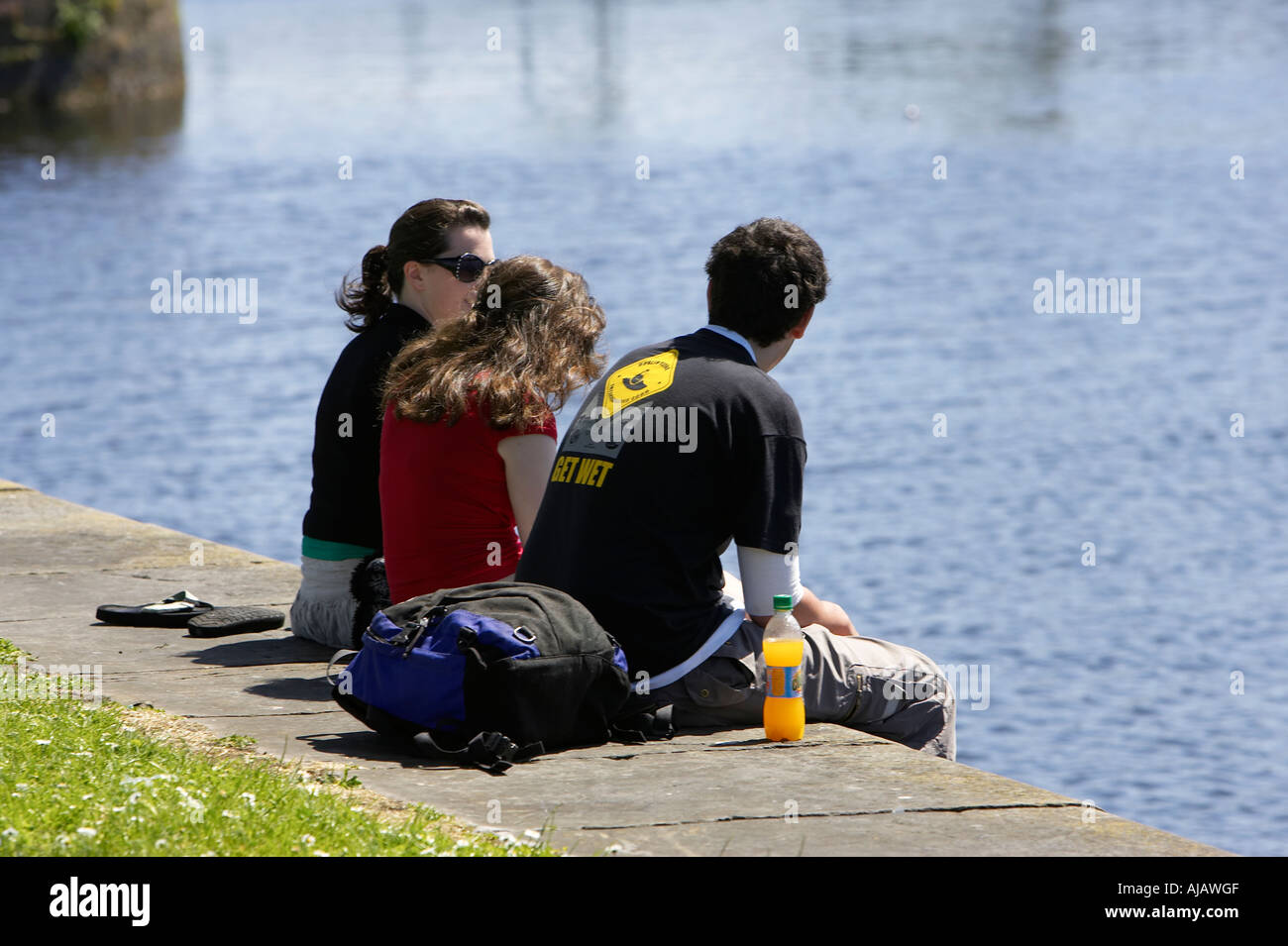 group of three young people enjoying the sunshine on the quay next to the corrib river on a sunday afternoon Stock Photo