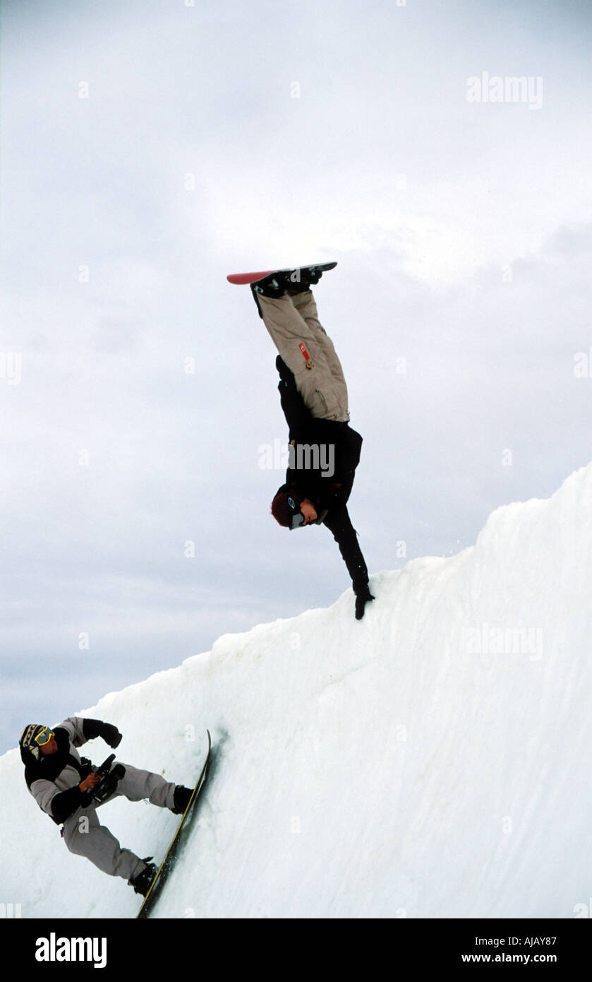 Female snowboarder performing hand stand hand plant whilst being filmed Stock Photo