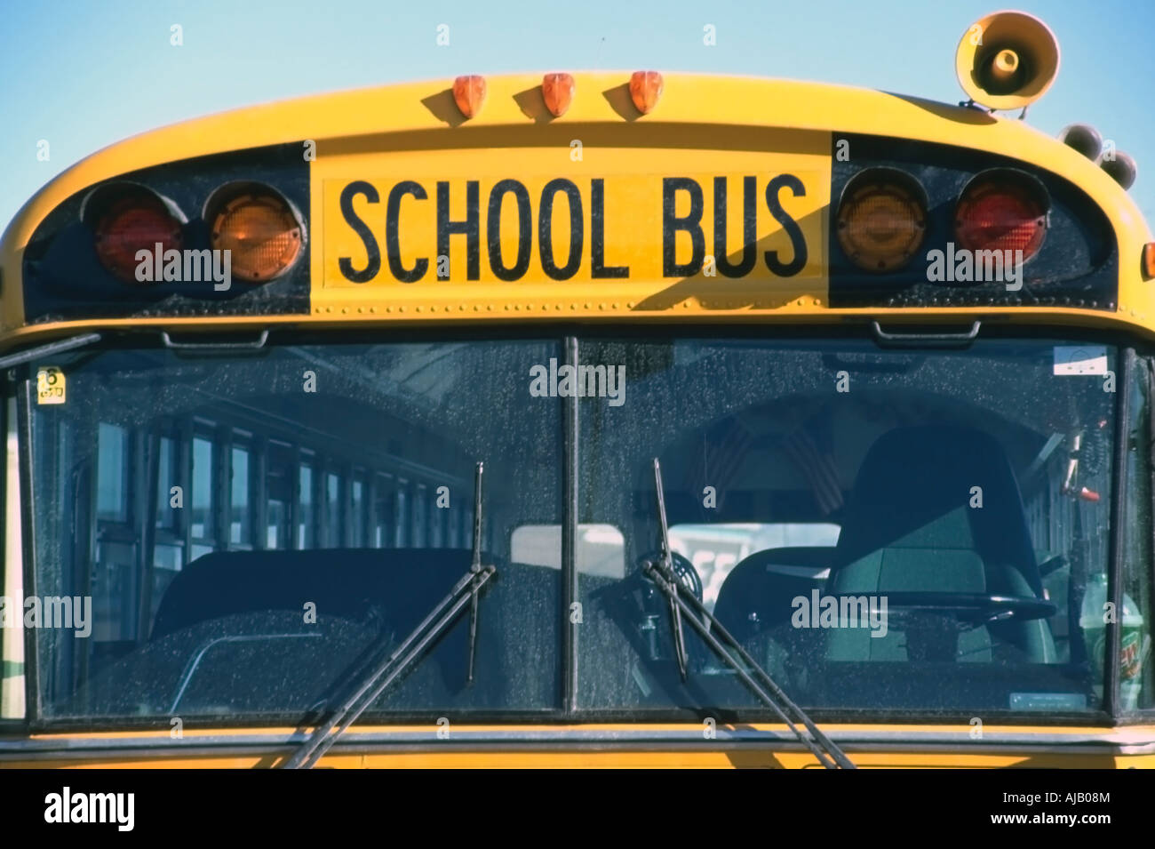 A head on, up close view of a bright yellow school bus. Its' windshield dominates the frame, with the words 'school bus' bold. Stock Photo