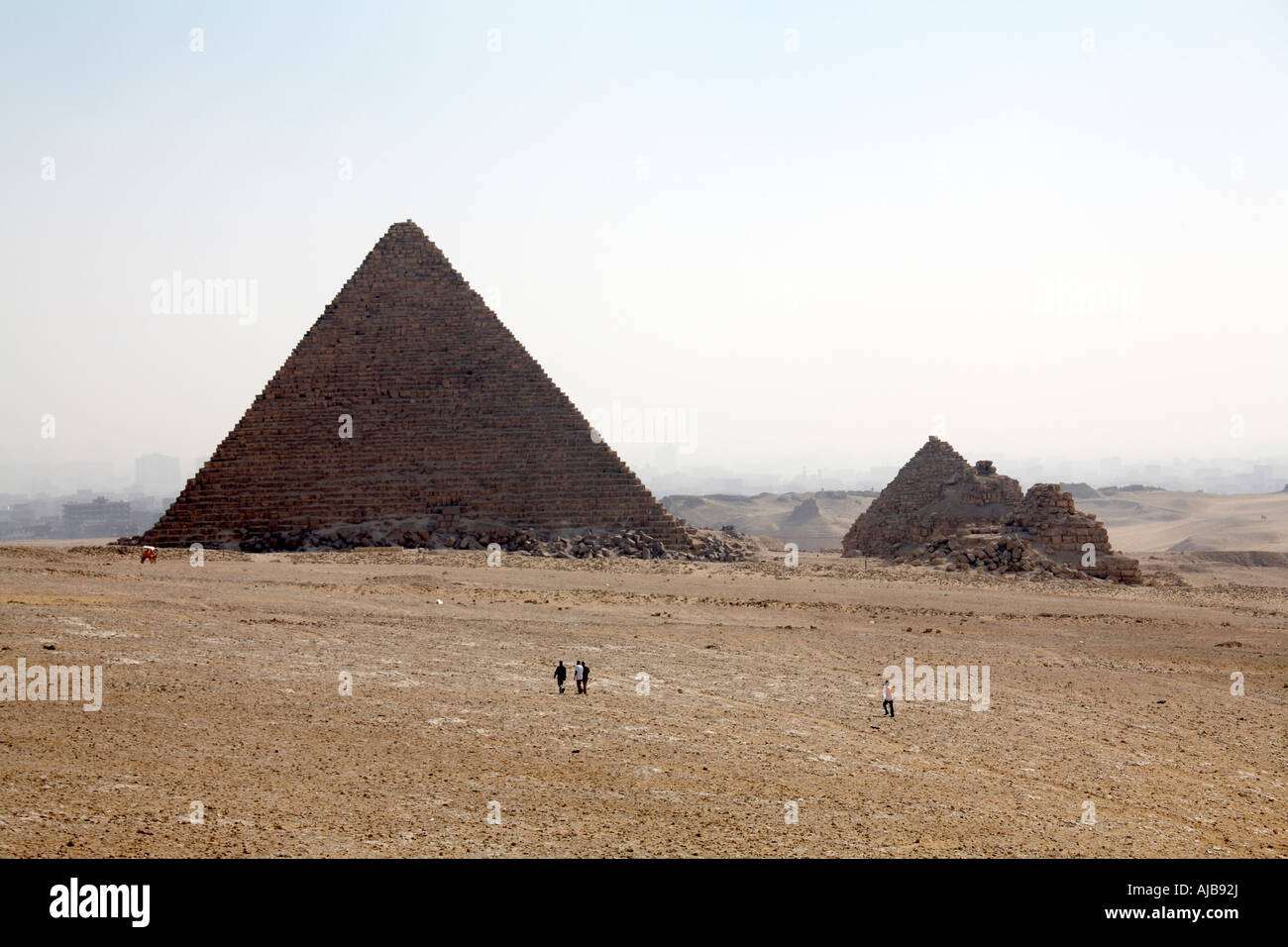 Pyramid of Menkaure Mycerinus and smaller Queen s pyramids with people walking in stony desert Giza Cairo Egypt Africa Stock Photo