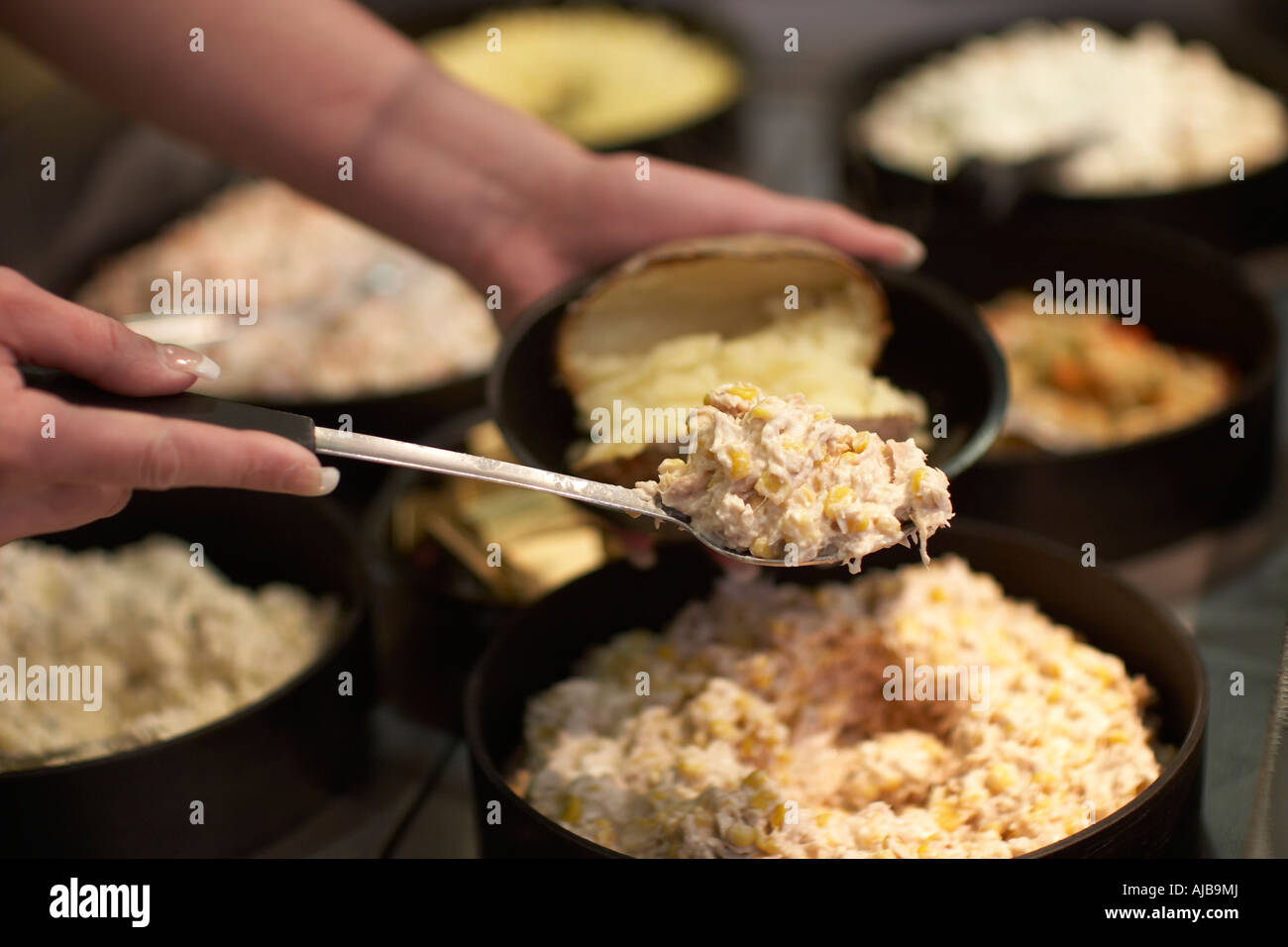 Woman person serving baked jacket potatoes or potato food putting in tuna sweetcorn mayonaise filling with spoon Stock Photo