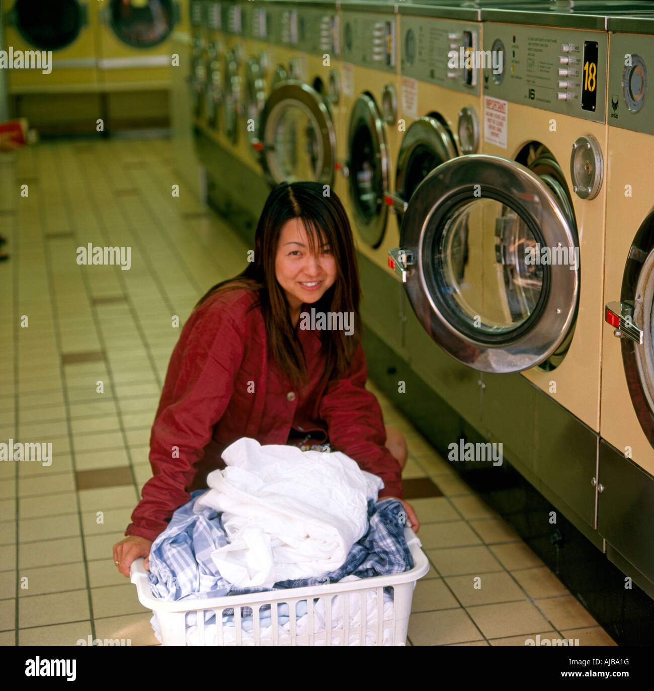 Asian woman smiling in a laundrette with a clothes basket of laundry