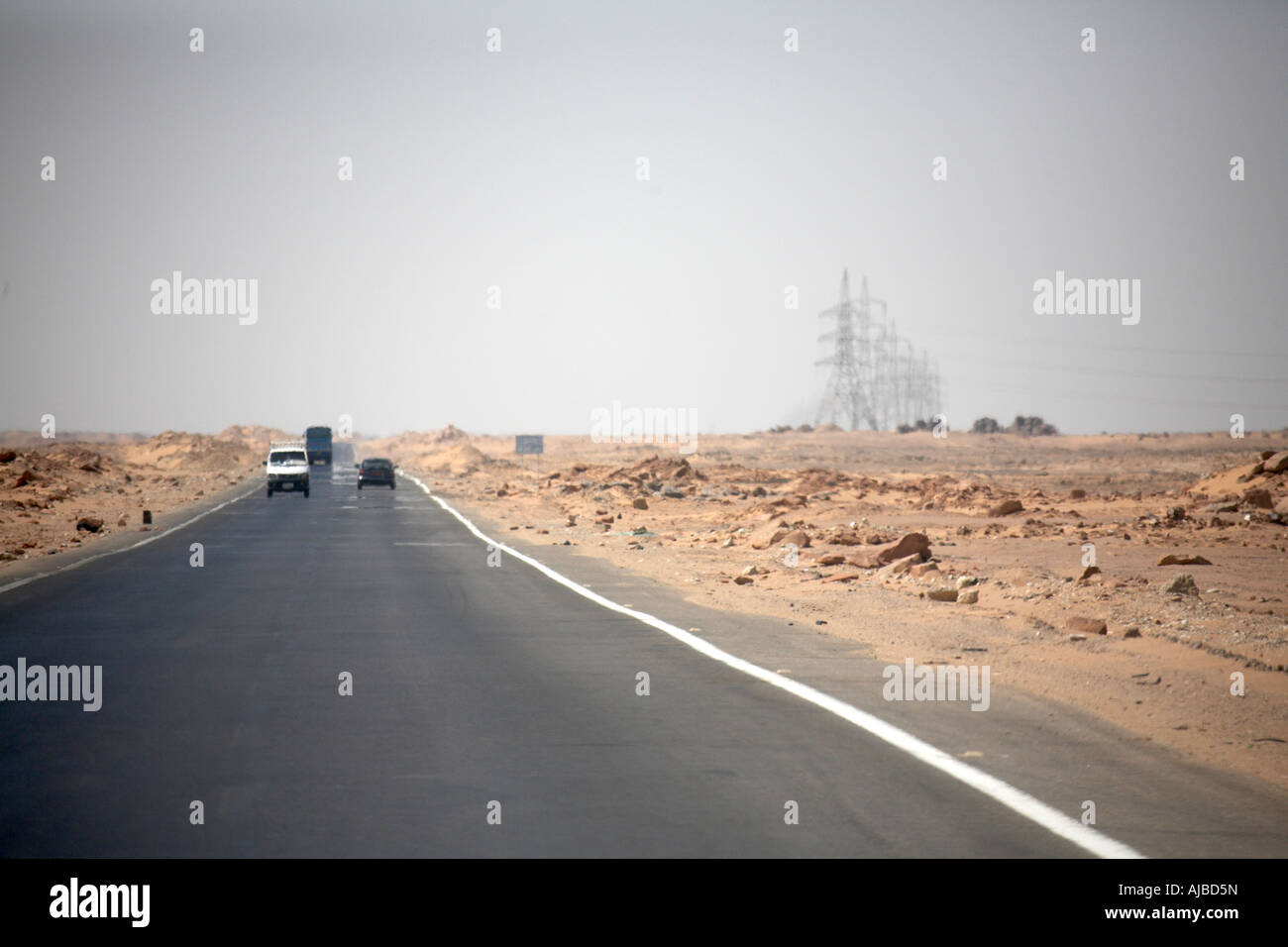 Traffic on desert road and electric transmission power cable pylons carrying electricity  southern Egypt Africa Stock Photo