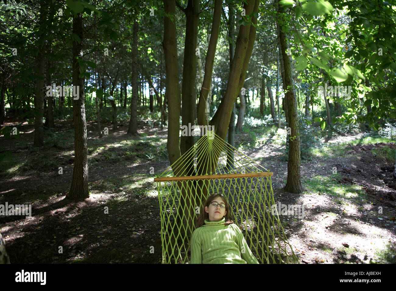 An eleven year old girl sleeps in a hammock wearing matching green to surrounding trees Little Dewchurch Herefordshire England Stock Photo