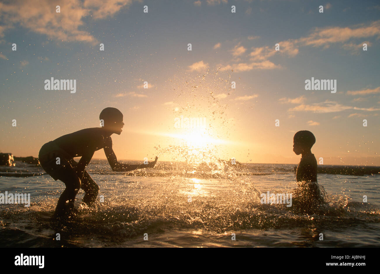 Two Boys Playing in Surf, Silhouetted at Dusk Stock Photo