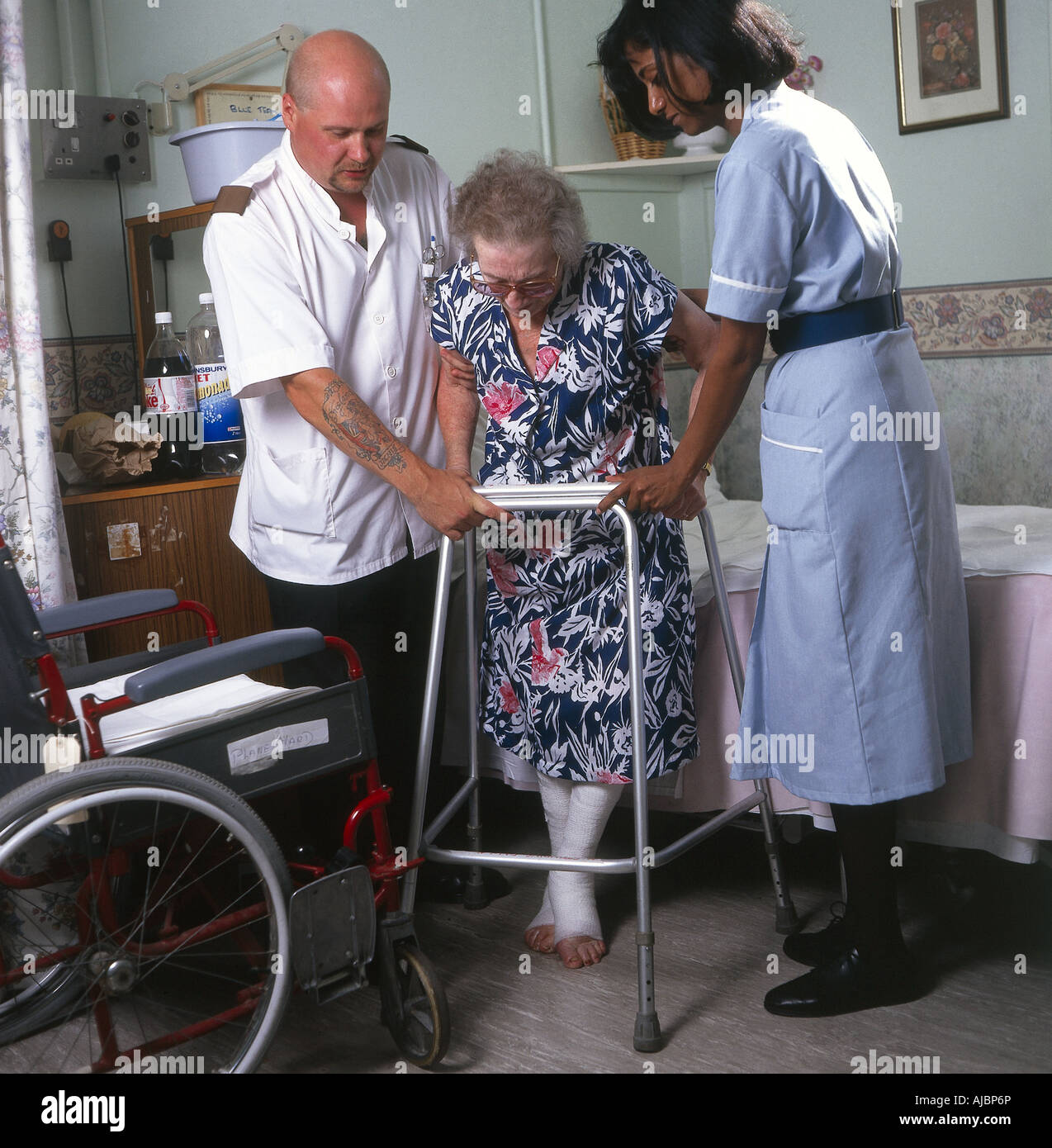 An elderly patient using a Zimmer frame with the assistance of medical