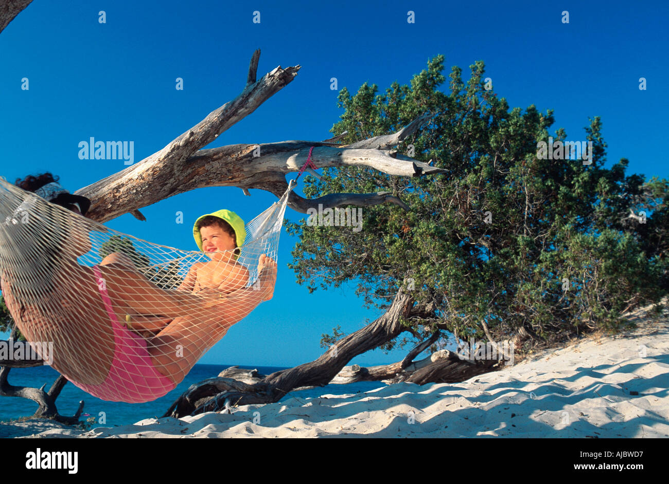 mother and sun lying on hammock, woman wearing pink swimsuit, boy wearing green hat, looking at each other Stock Photo
