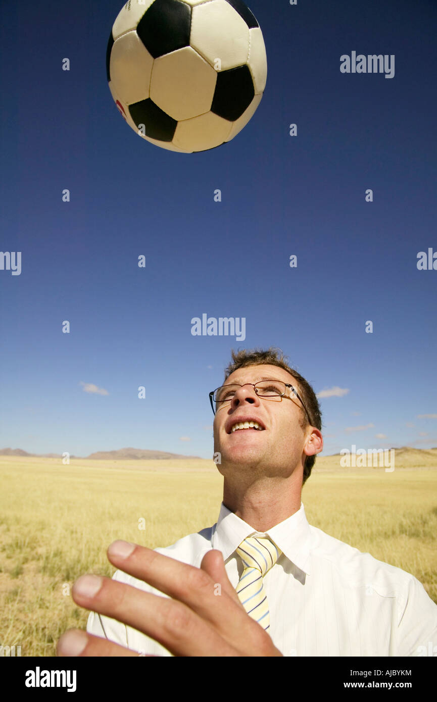 Businessman in a Suit Playing with a Soccer Ball in a Desert Stock Photo