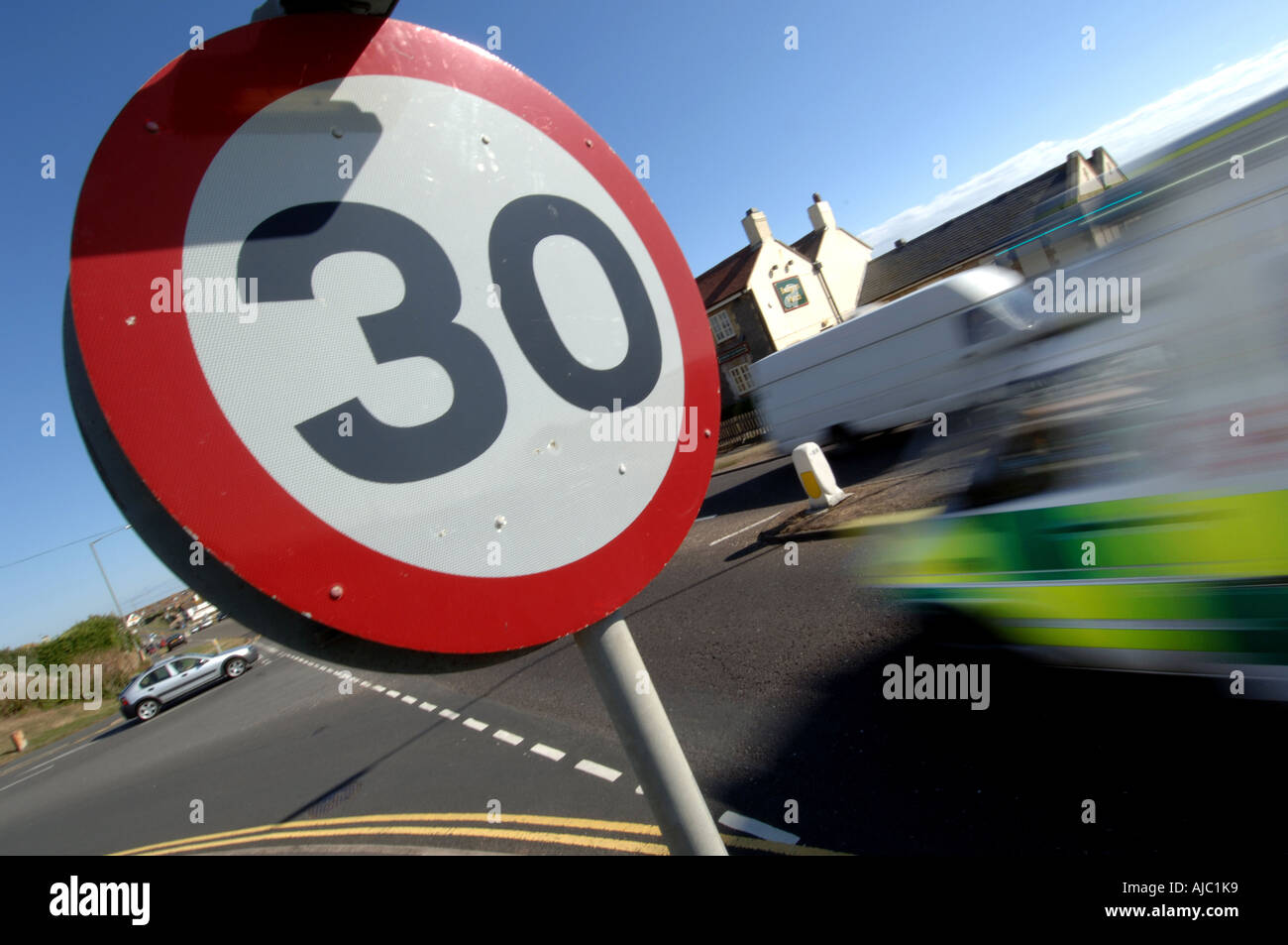 An ambulance races into a 30 mph miles per hour speed limit area marked by a 30 mph warning sign at a road junction. Stock Photo