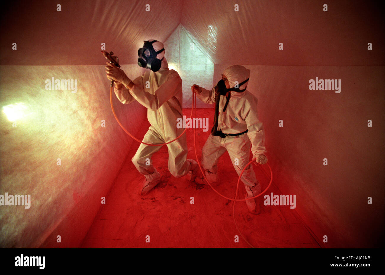 Two performance artists in white boiler suits and masks spray red paint. Stock Photo