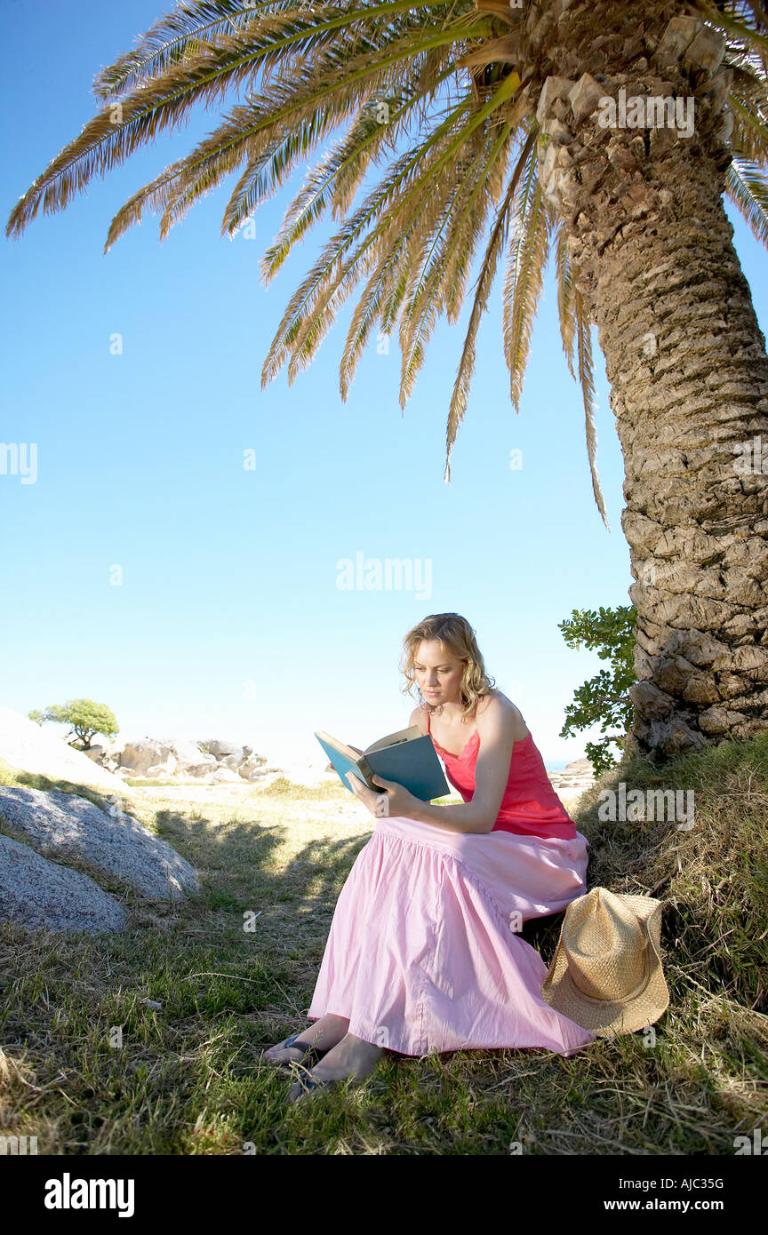 Young Woman Reading a Book Under a Palm Tree Stock Photo