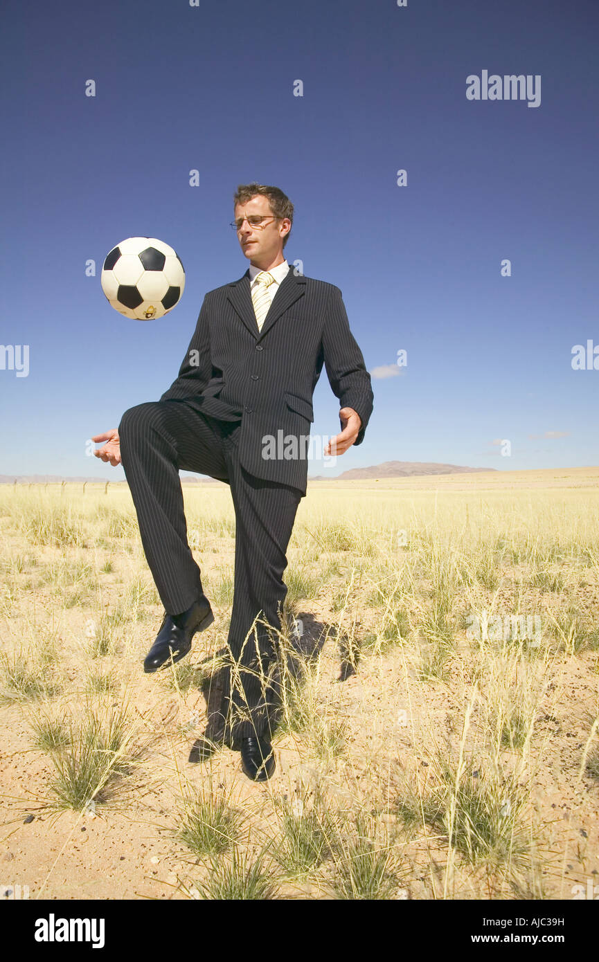 Businessman in a Suit Playing with a Soccer Ball in a Desert Stock Photo