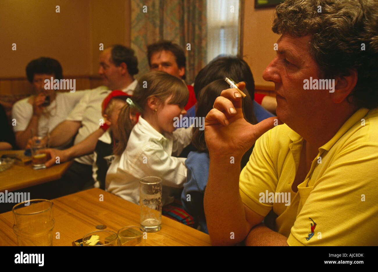 A father smokes lit cigarette indoors in front of children and friends during a night out in their local pub in Tarbet, Scotland Stock Photo