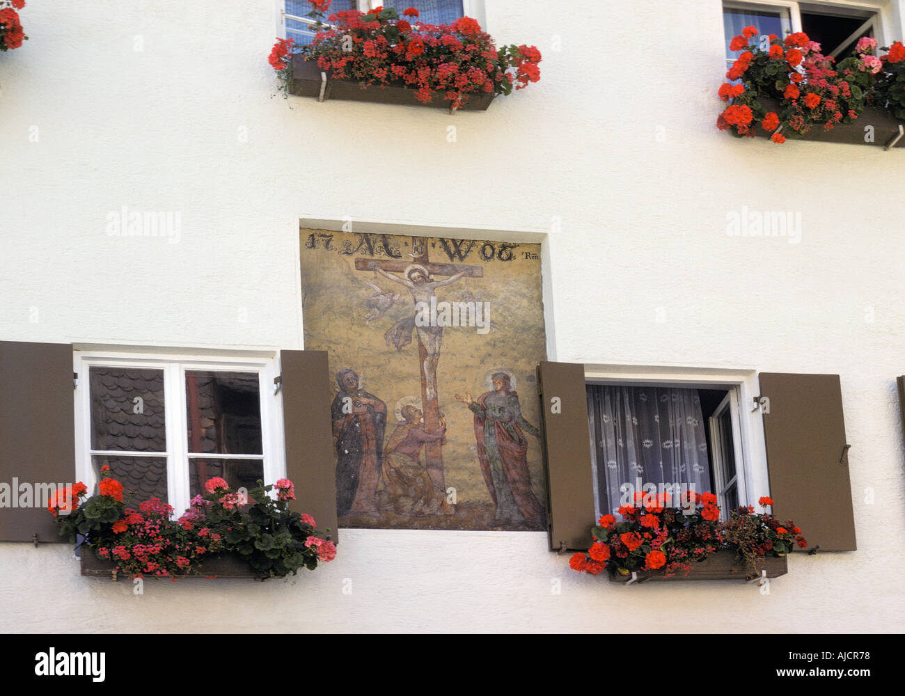 Geranium filled window boxes and a painting of the Crucifixon decorate the facade of a house in Fuessen Bavaria Germany Stock Photo