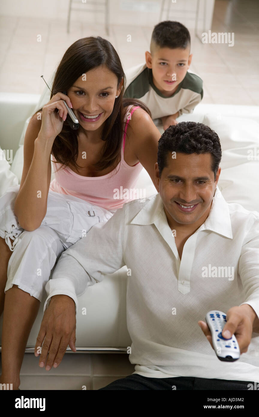 Family sitting on sofa watching TV, mother on mobile phone Stock Photo