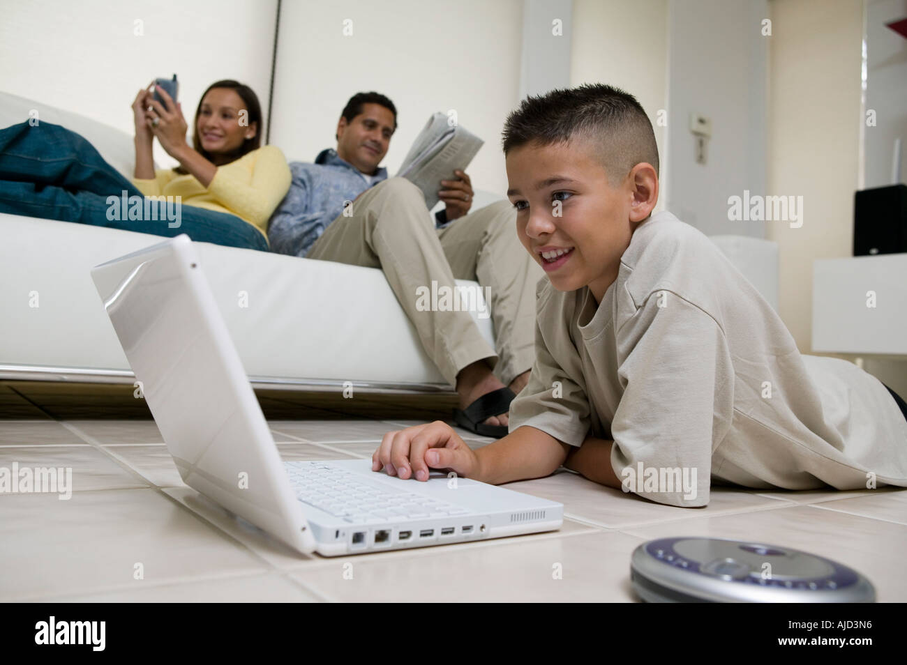 Boy Using Laptop on Floor in living room, mother and father on sofa, ground view Stock Photo