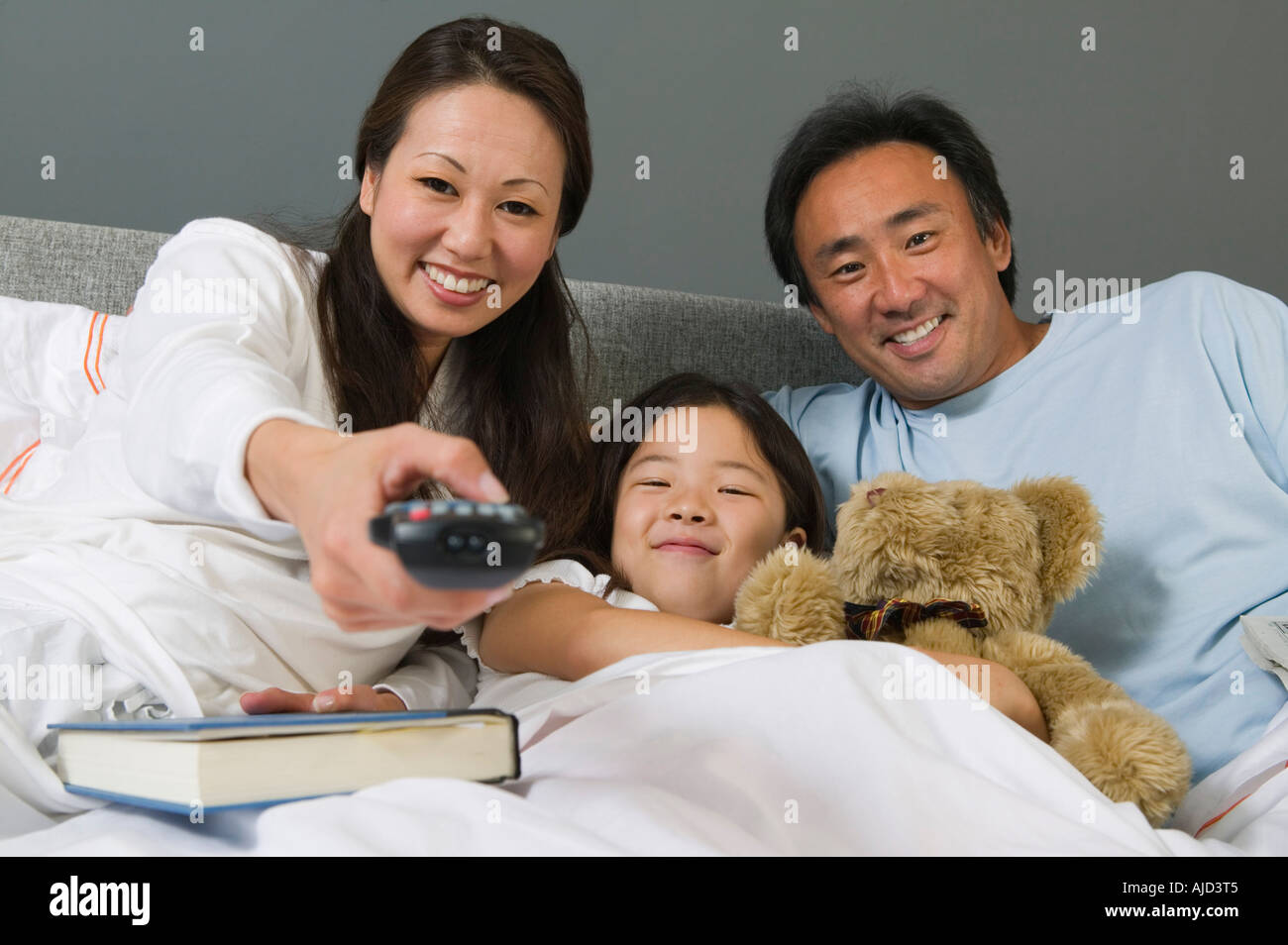 Family Watching TV Together in Bed, mother using remote control Stock Photo