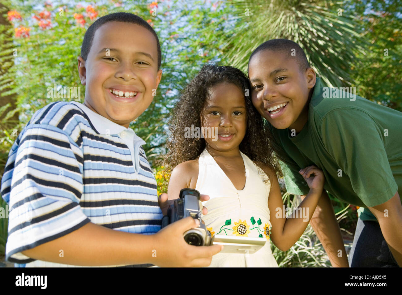 Boy (7-9) holding camcorder, with younger sister (5-6) and older brother (10-12), portrait. Stock Photo