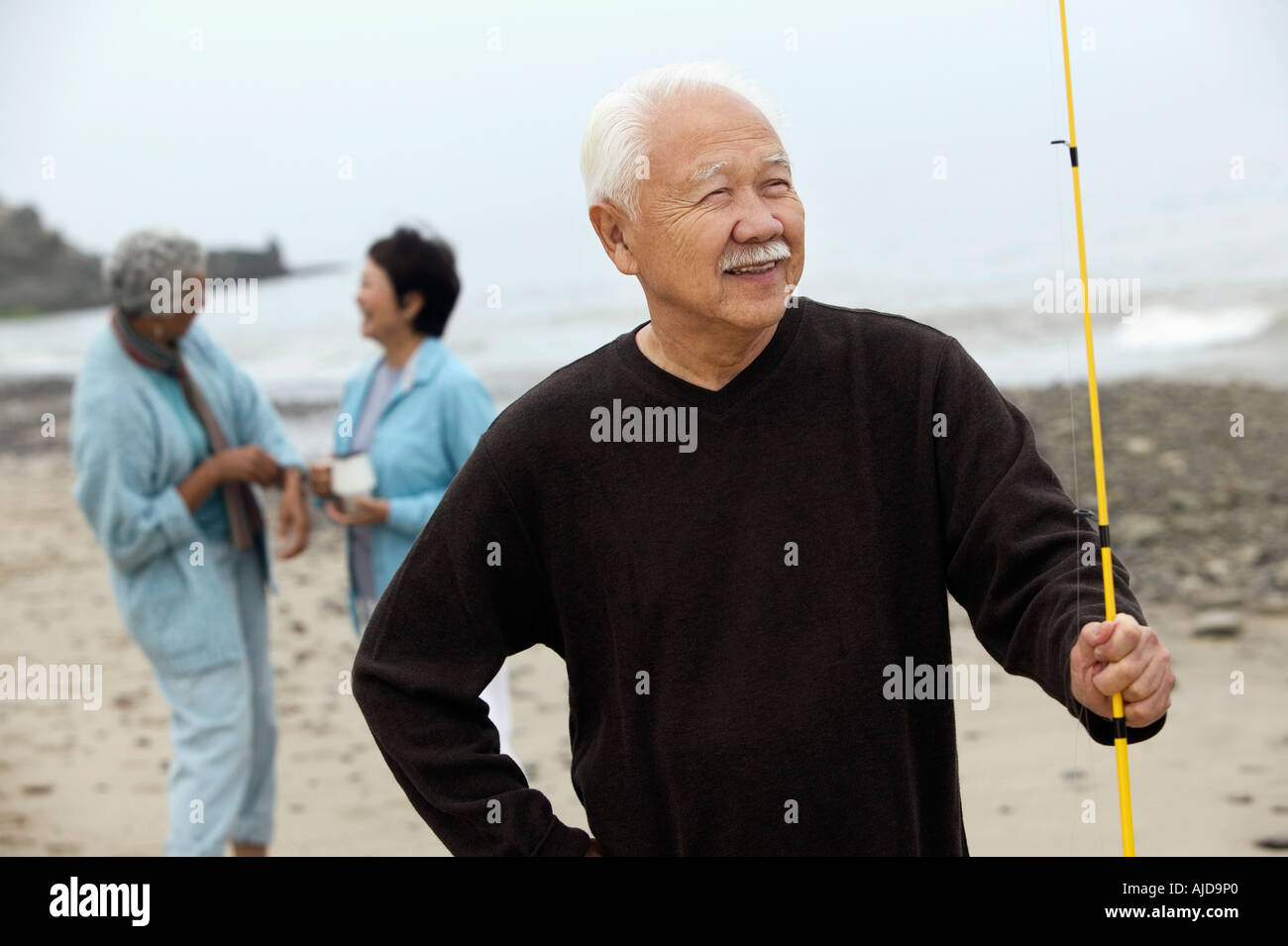 Asian Fisherman on beach holding fishing rod whilst friends talk in the  background Stock Photo - Alamy
