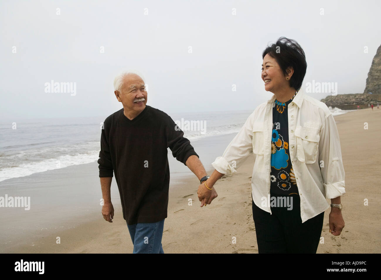 Mature couple holding hands, walking on beach Stock Photo