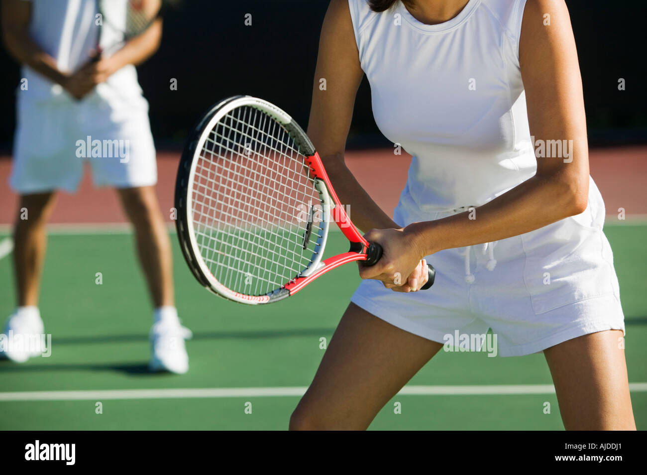 Mixed doubles tennis players on court, focus on woman, mid section