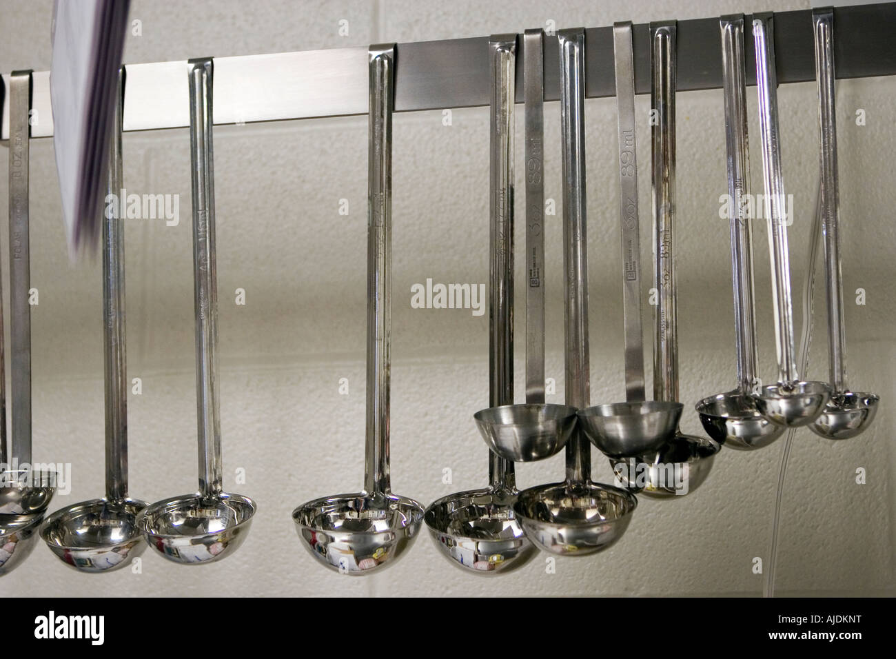 Various size ladles hanging from rack in school kitchen Stock Photo