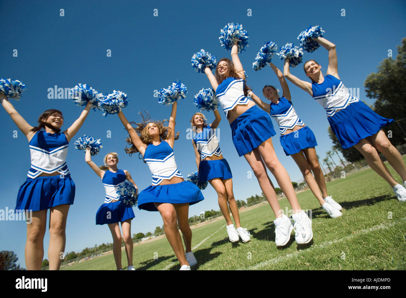 Low angle view of cheerleaders jumping with pom poms raised against