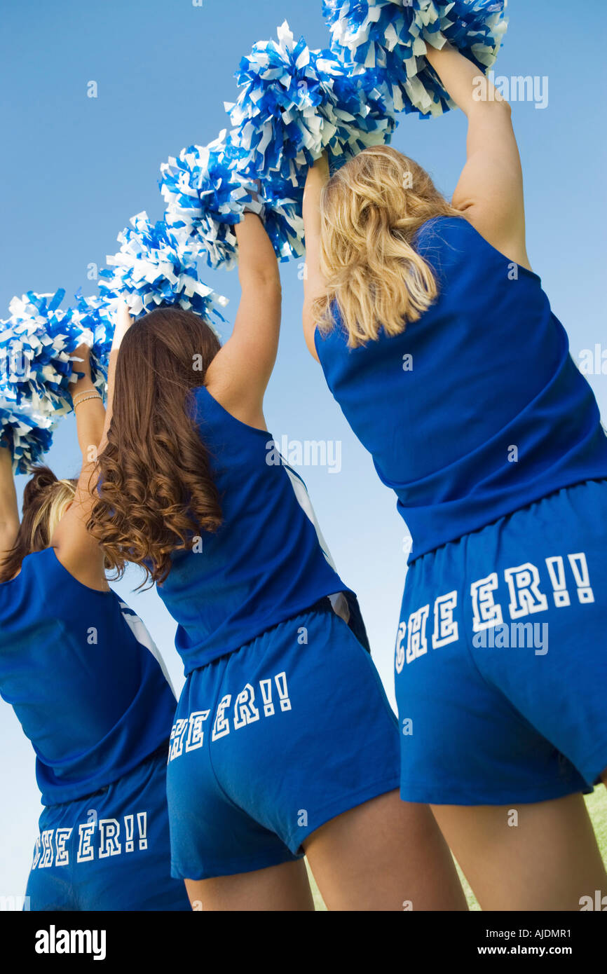 Three Cheerleaders rising pom-poms, rear view Stock Photo