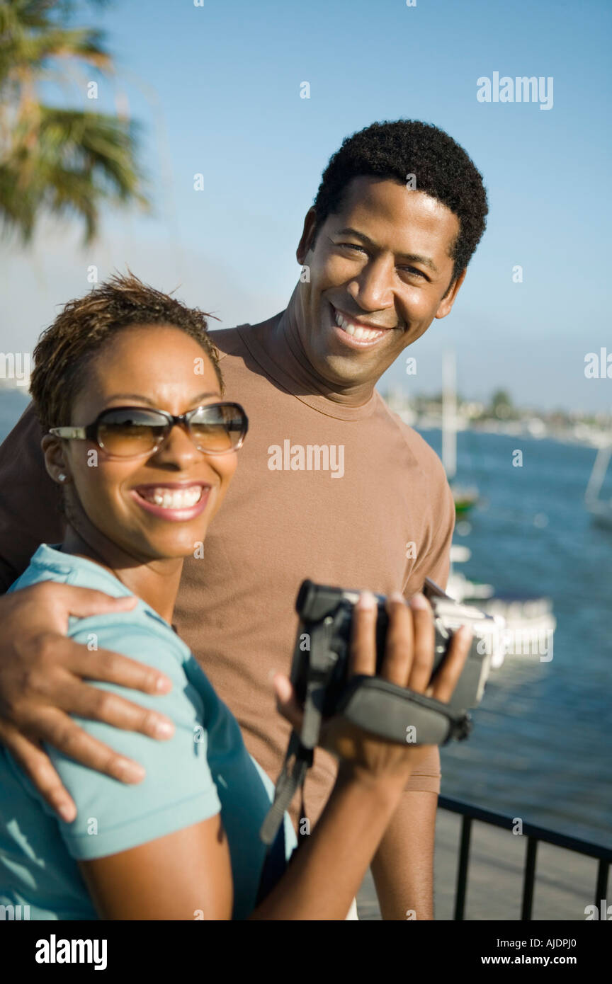 Couple with video camera at marina, (portrait) Stock Photo