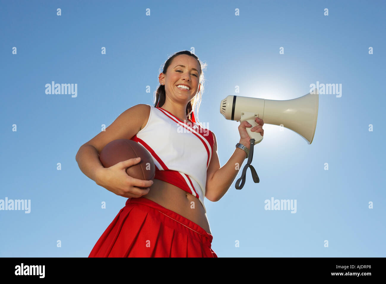 Cheerleader Holding Football and Megaphone, low angle view, portrait, (portrait), (low angle view) Stock Photo