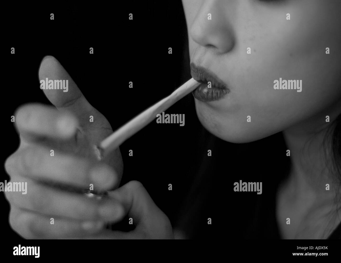 young asian  woman with painted lips lighting a large roll up cigarette Stock Photo