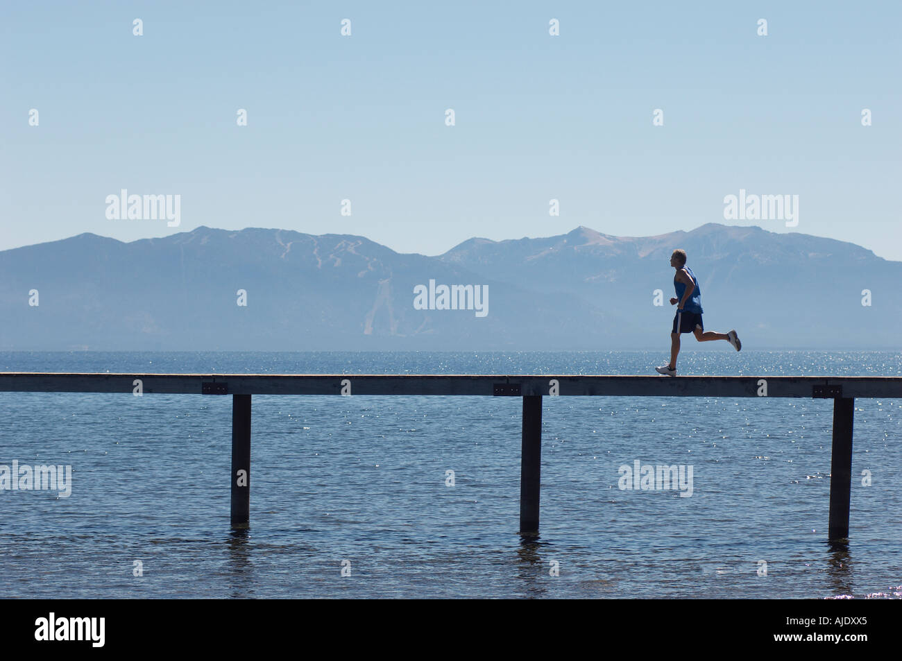 Man running along pier with mountains behind, side view Stock Photo