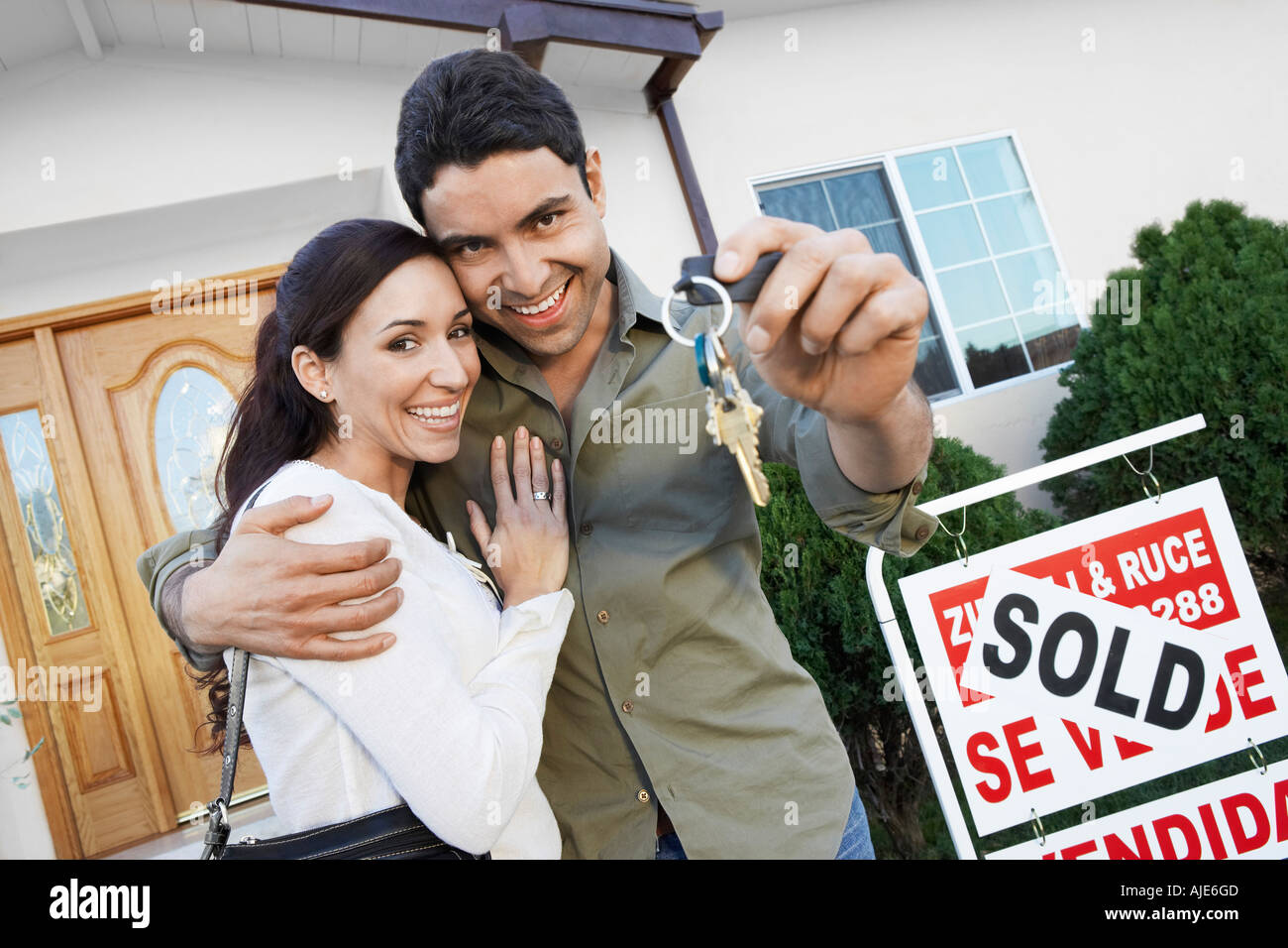 Homeowners standing in front of house with Sold sign holding key ...