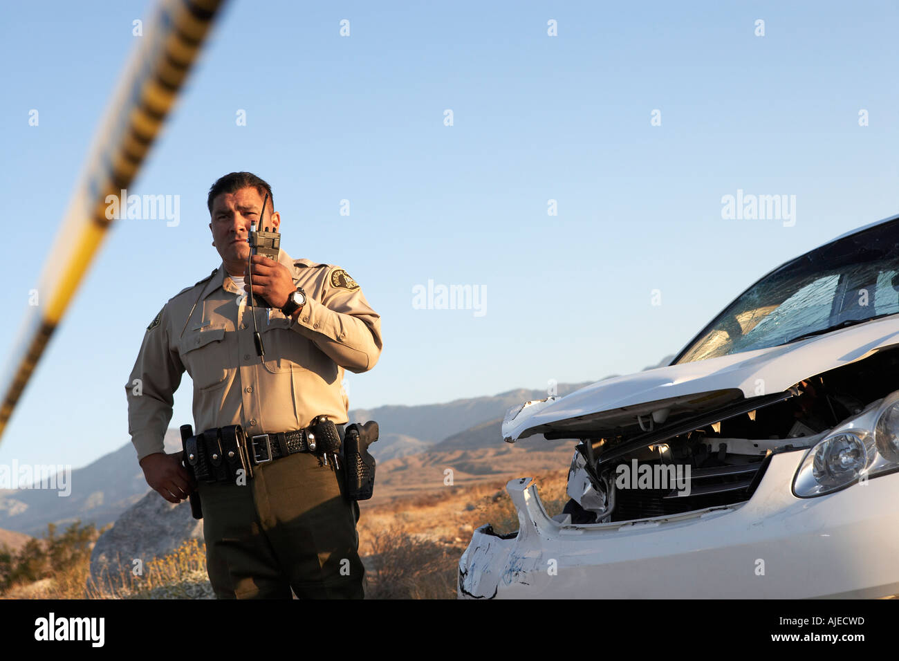 Police officer using walkie-talkie next to wrecked car Stock Photo