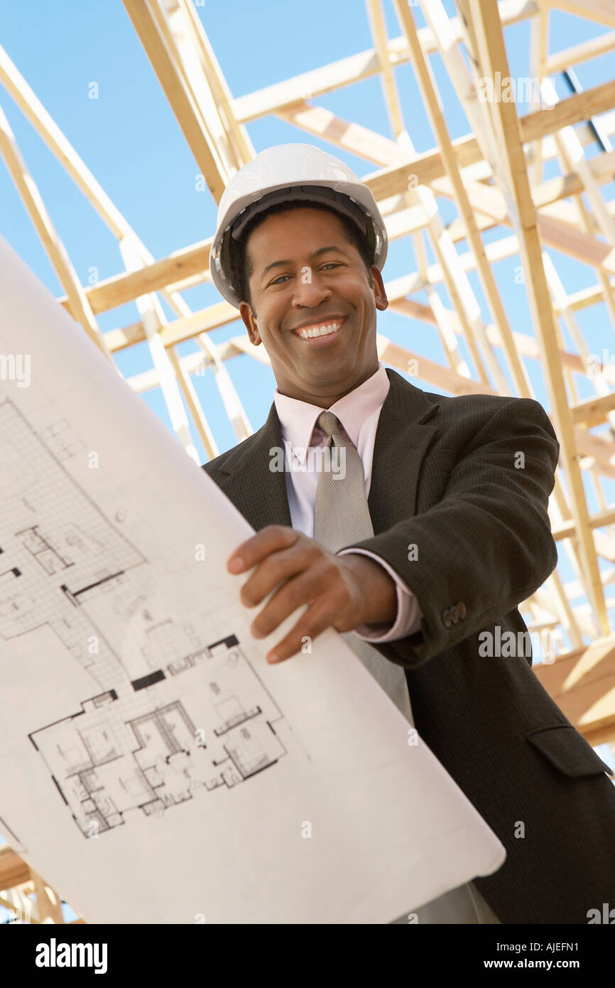 Smiling Surveyor in hard hat with building plans on Construction Site