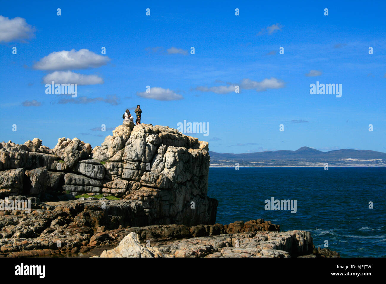 Tourists standing on rocks and enjoying whale watching and wonderful ocean views of Walker Bay in Hermanus, South Africa on sunny day with blue sky Stock Photo