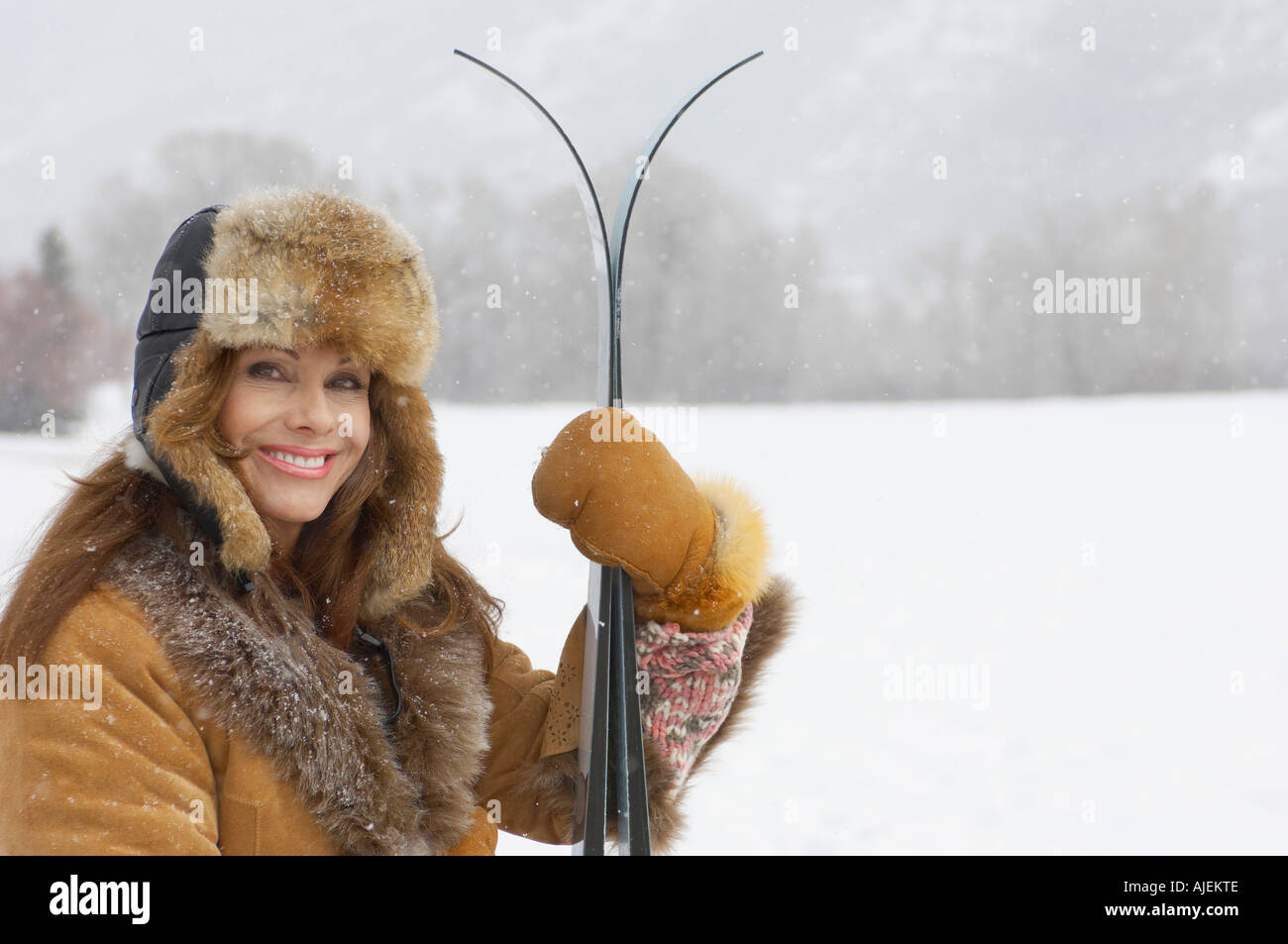 Woman wearing fur coat and hat, holding skis, in snow covered field, portrait. Stock Photo