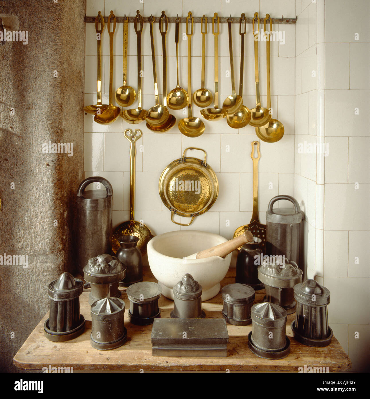 Various kitchen utensils including brass ladles and a pestle and mortar displayed on a wooden