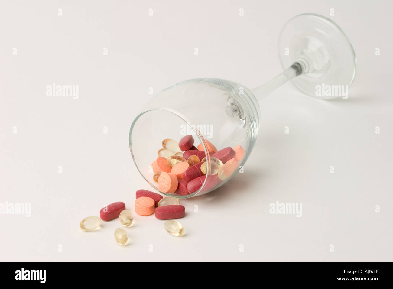 Assorted vitamin pills spilling out of wine glass Stock Photo