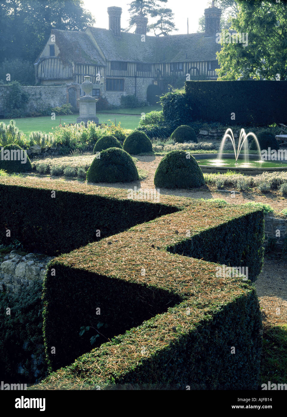 The garden at Ightham Mote Kent in November looking over the topiary towards a small fountain stone urn on the lawn Stock Photo
