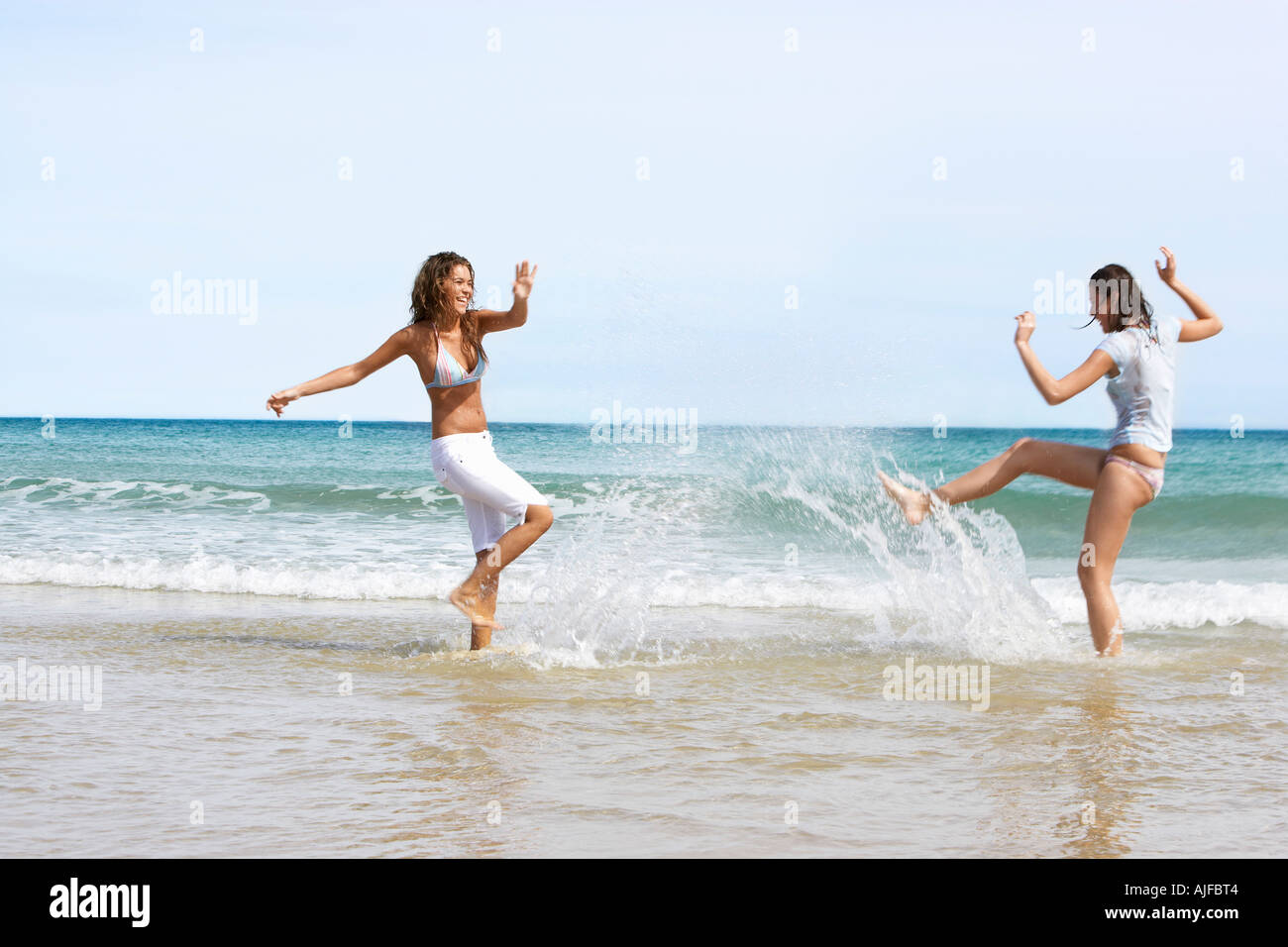 Two Young Women Splashing Each Other on Beach Stock Photo