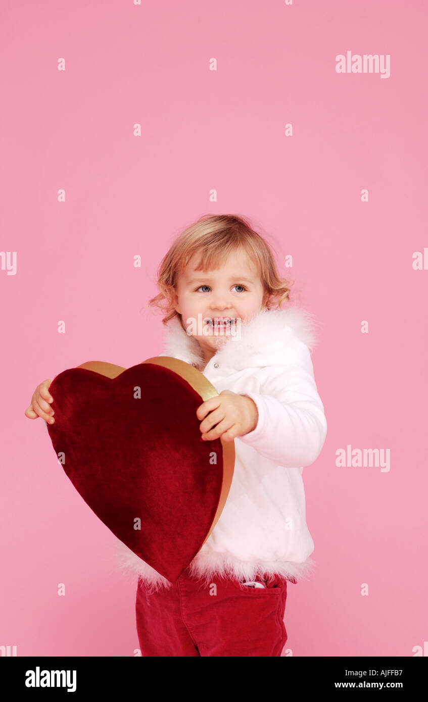 Two year old girl holding red velvet covered valentines day heart Stock Photo