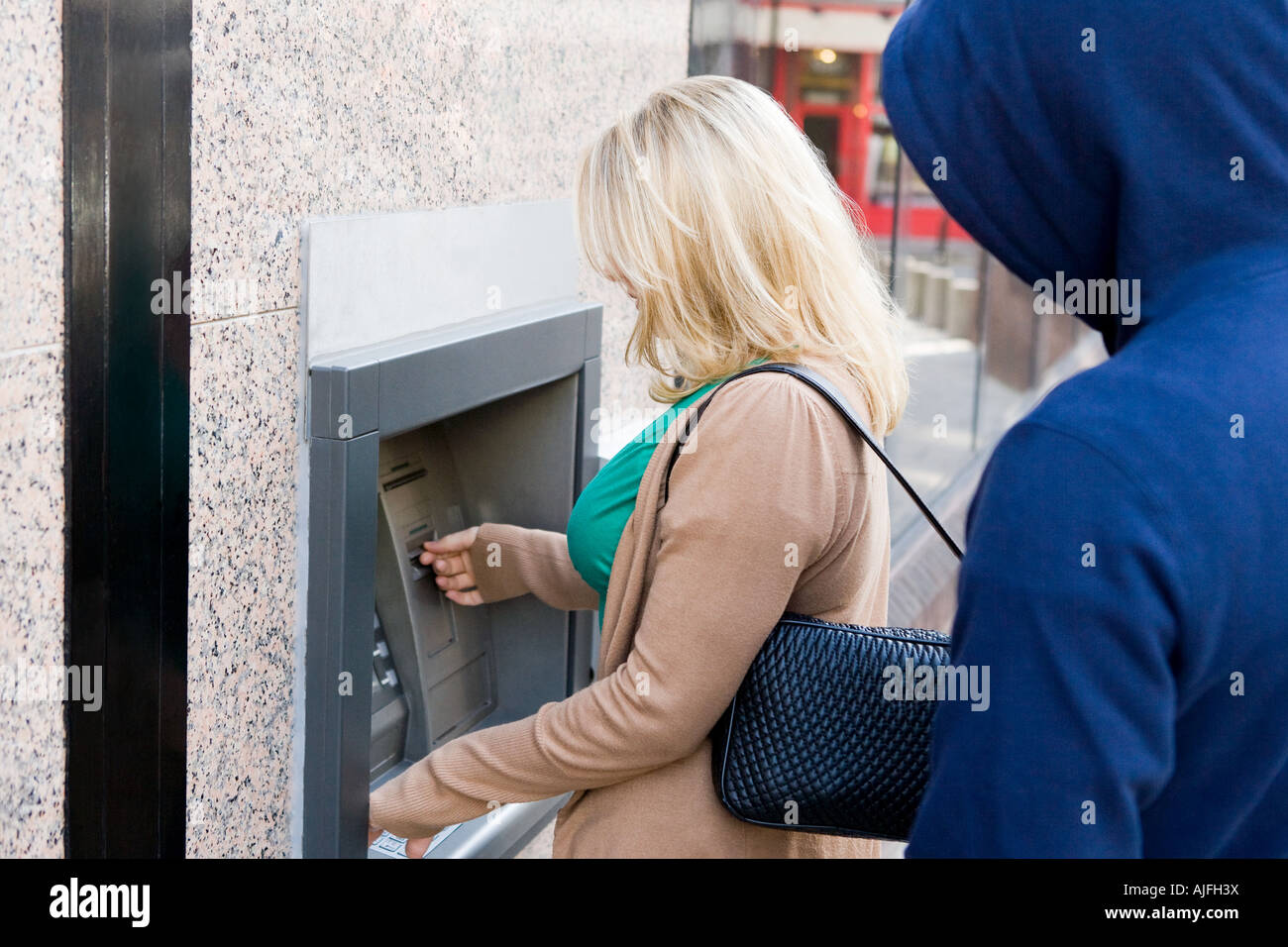 Thief looking over womans shoulder at cash machine Stock Photo