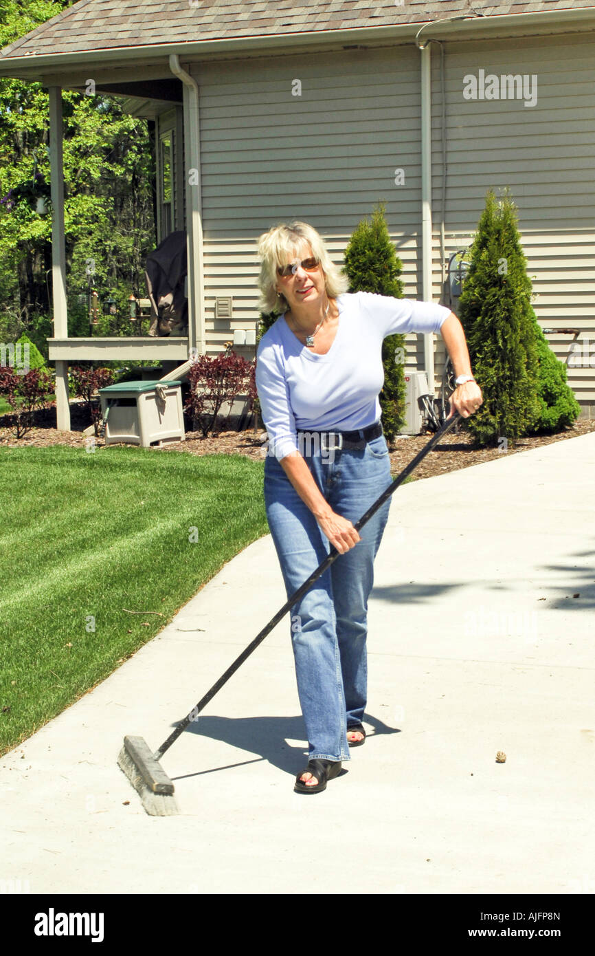 Attractive female sweeping the driveway clean outside her home Stock