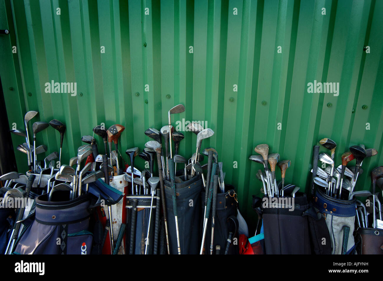Sets of old golf clubs standing against a wall at a recycling centre in