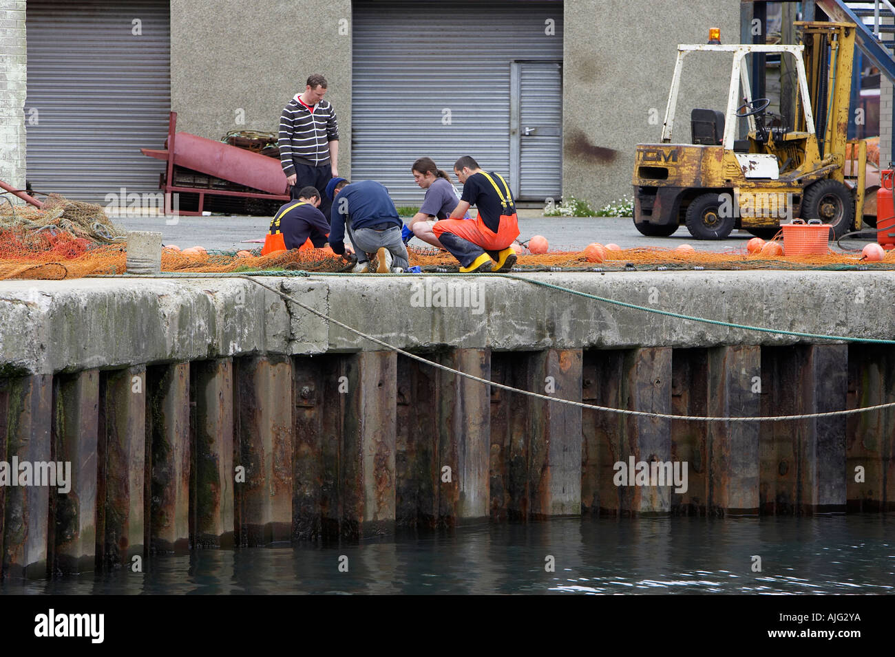 fishermen repair their fishing nets on the quay side kilkeel harbour county down northern ireland Stock Photo