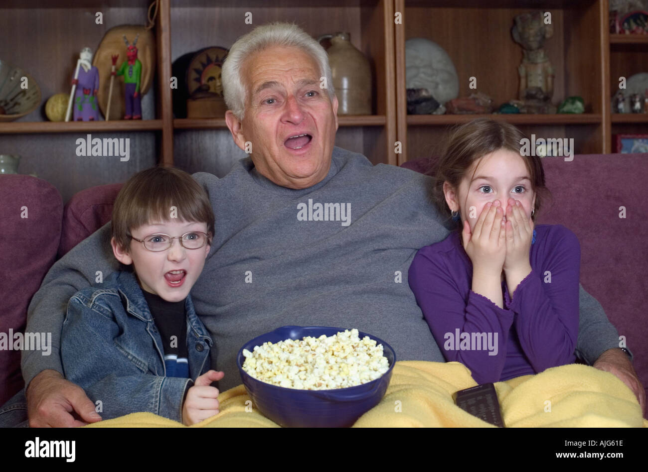 Grandfather and grandchildren watching scary movie on television eating popcorn Stock Photo